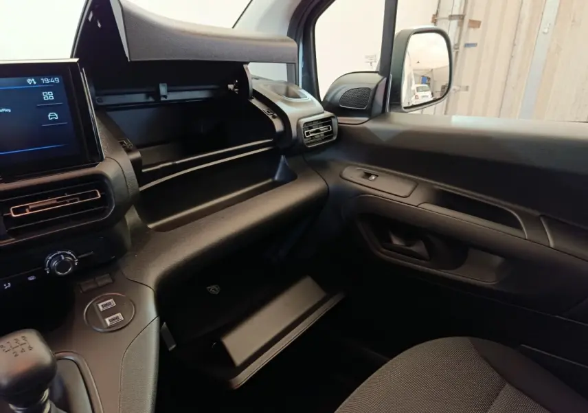 Intérieur du Peugeot Partner 2025 blanc, vue côté passager avec boîte à gants ouverte et tableau de bord moderne.