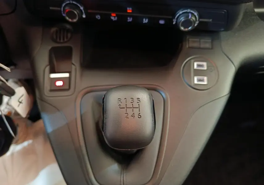 Gros plan sur le levier de vitesses manuel noir du Peugeot Partner blanc 2025, avec commandes et ports USB visibles.