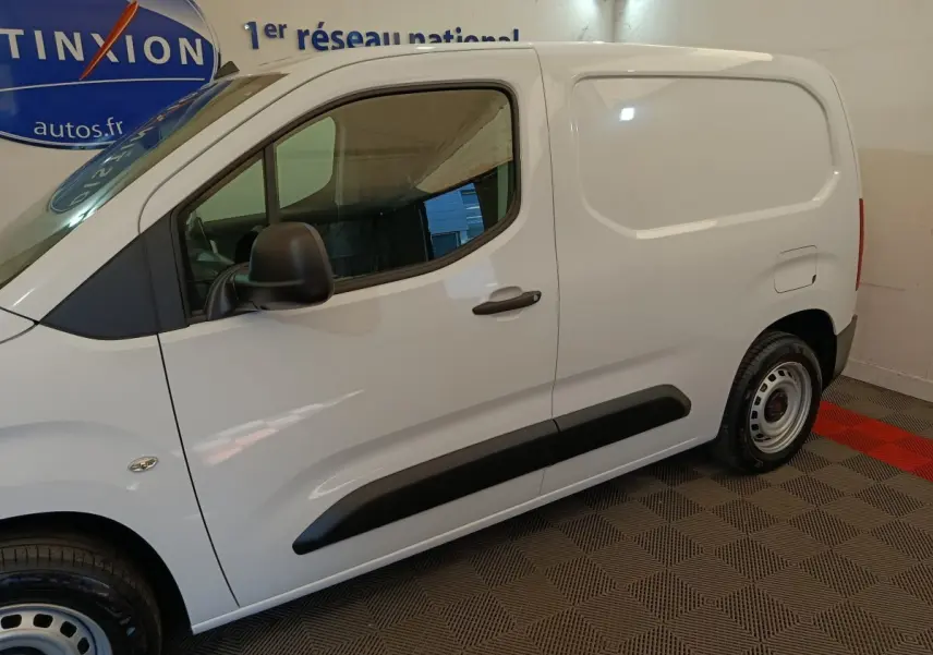 Vue de profil côté gauche du Peugeot Partner blanc, mettant en valeur la porte latérale pleine et les protections noires.