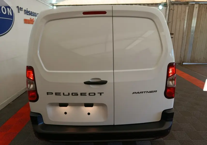 Vue arrière d'un utilitaire blanc Peugeot Partner avec portes battantes et feux arrière allumés en intérieur.