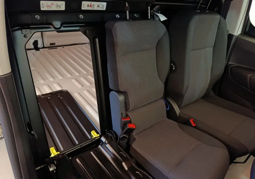 Vue intérieure du Peugeot Partner blanc 2025 montrant les sièges avant et l’espace de chargement derrière la cloison pleine.