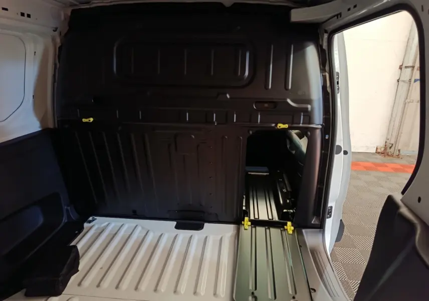 Vue intérieure arrière du Peugeot Partner blanc 2025 montrant la cloison pleine avec trappe de passage et plancher métallique.