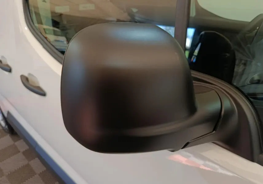 Rétroviseur noir en gros plan sur le côté gauche d’un Peugeot Partner blanc, vue latérale partielle.