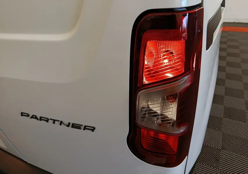 Gros plan sur le feu arrière droit et le logo PARTNER du utilitaire Peugeot blanc, vue arrière droite.