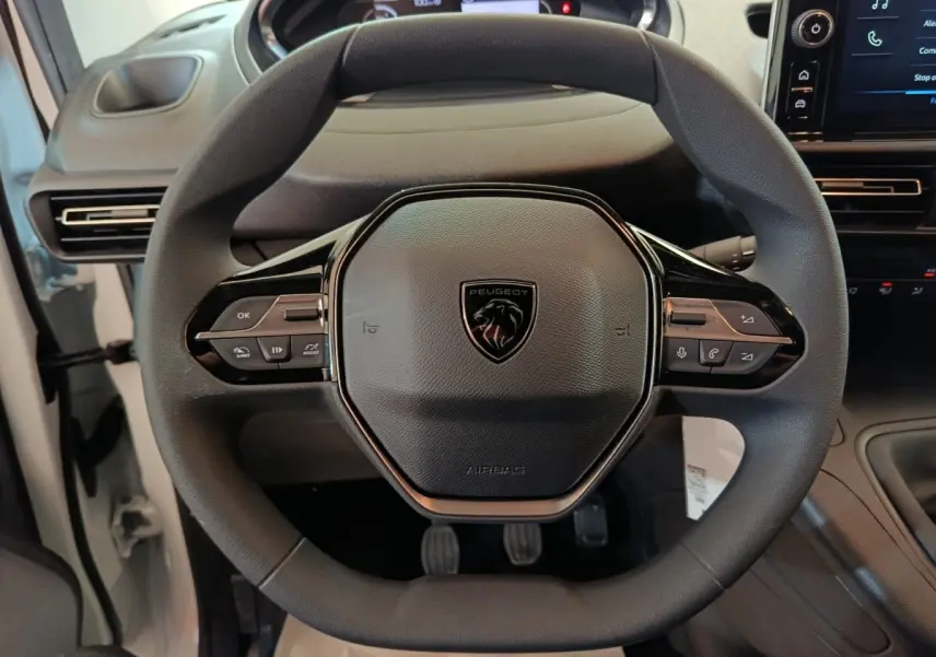 Vue rapprochée du volant noir du Peugeot Partner 2025, avec commandes intégrées et tableau de bord partiellement visible.