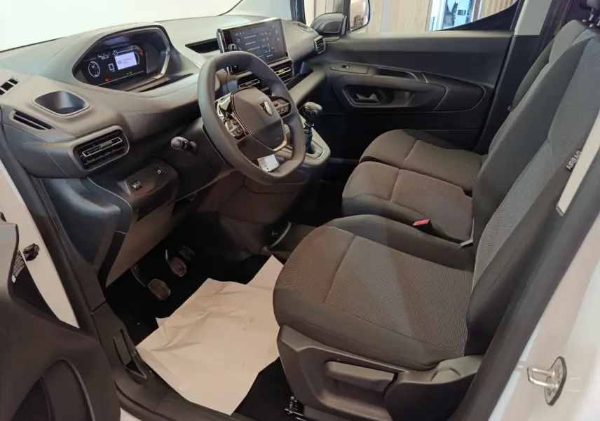 Intérieur côté conducteur du Peugeot Partner blanc 2025, montrant tableau de bord, volant et sièges tissu gris.