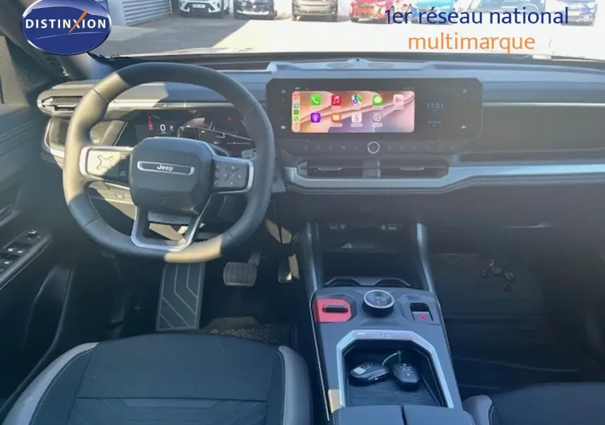 Vue intérieure avant du Jeep Compass 2026, tableau de bord et volant noirs avec écran tactile central allumé.