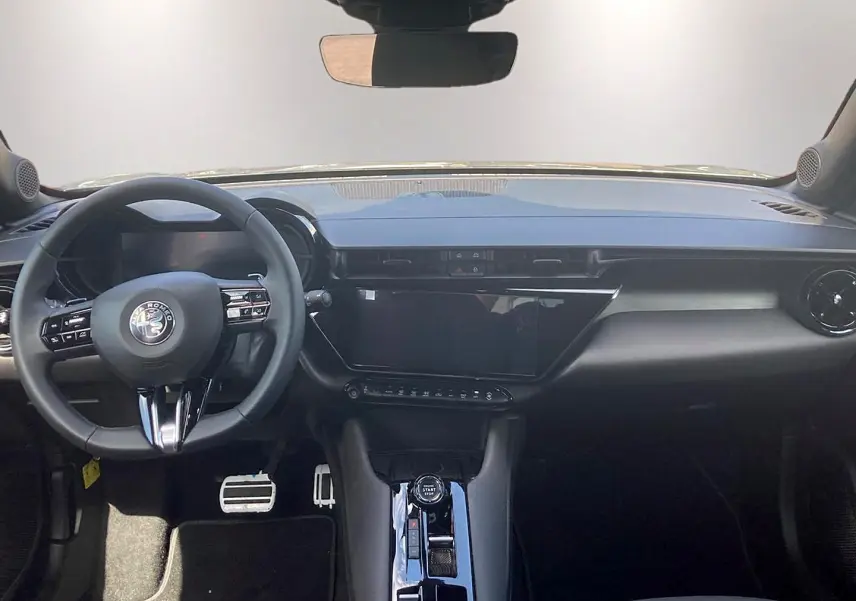 Vue intérieure frontale de l'Alfa Romeo Junior 1.2 hybride, tableau de bord noir avec écran tactile et volant multifonction.