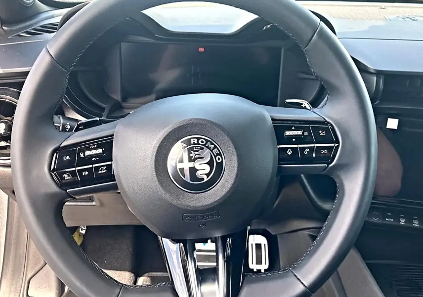 Vue rapprochée du volant noir de l'Alfa Romeo Junior 1.2 hybride 2026, avec logo central et commandes intégrées.