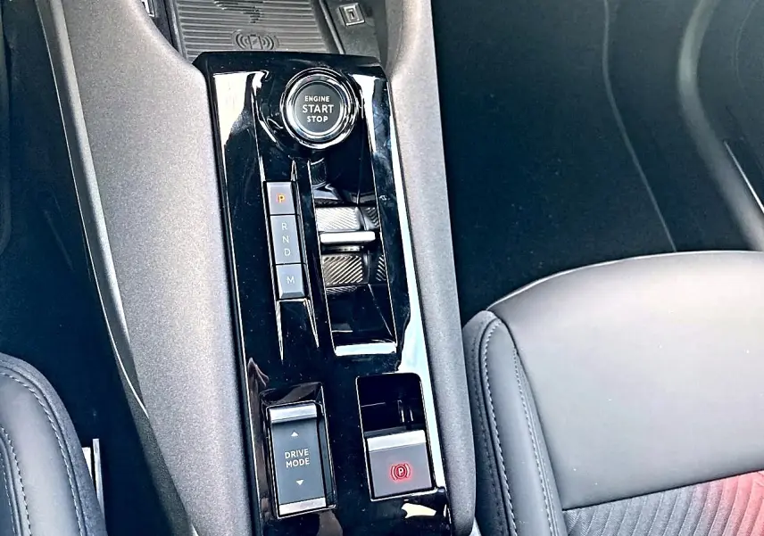 Gros plan sur la console centrale noire brillante de l'Alfa Romeo Junior 1.2 hybride, avec bouton start/stop et levier de vitesses.