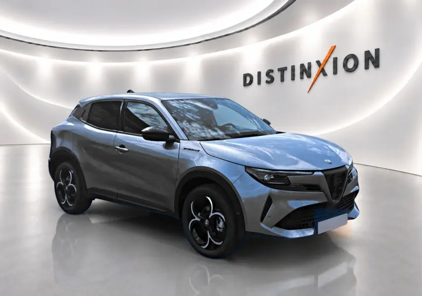 Alfa Romeo Junior gris en 3/4 avant droit, avec jantes alliage noires et vitres teintées dans un showroom lumineux.
