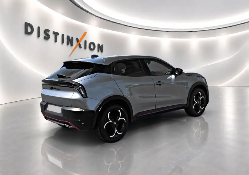 Vue 3/4 arrière droite d'une Alfa Romeo Junior gris métallisé avec jantes noires et toit noir dans un showroom lumineux.