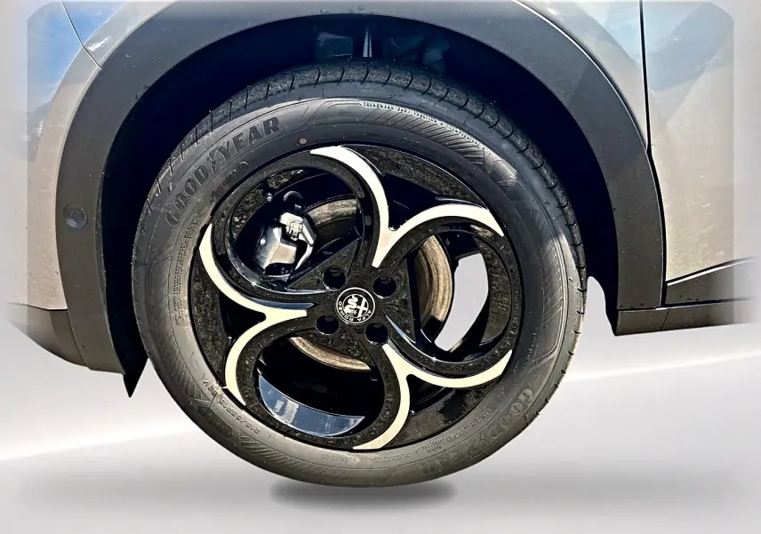 Gros plan sur la roue avant droite grise d’une Alfa Romeo Junior 1.2 hybride avec jante en alliage noir et argent.