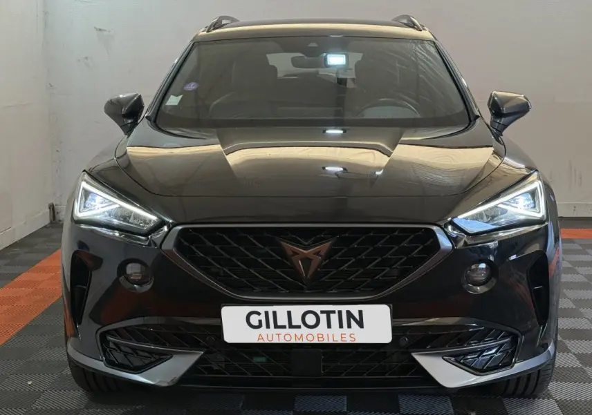 Vue frontale d'un CUPRA Formentor noir 2023 avec phares LED allumés et calandre distinctive au logo cuivre.