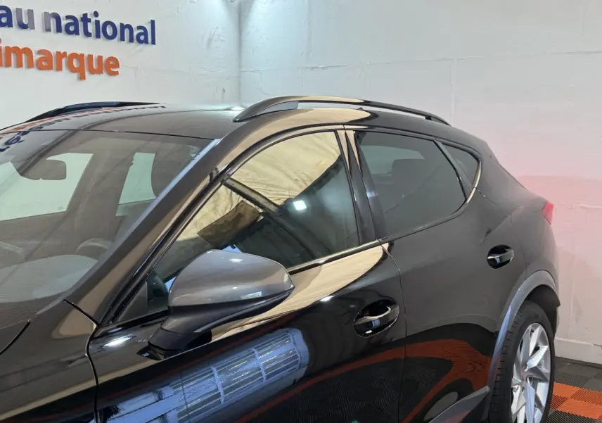 Profil côté gauche d'un CUPRA Formentor noir brillant avec rétroviseur et barres de toit visibles en intérieur showroom.