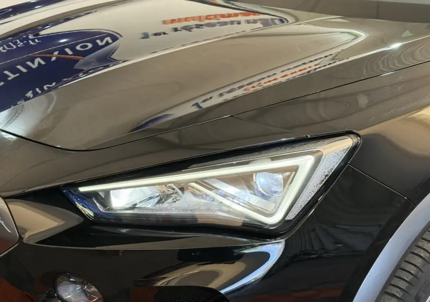 Gros plan sur le phare avant droit LED d'une CUPRA Formentor noire brillante avec capot lisse et reflet d'enseigne.