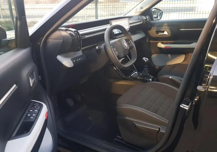 Intérieur avant gauche d’une Citroën C3 noire 2025, montrant le tableau de bord et les sièges tissu foncé.