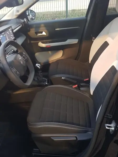 Vue intérieure côté conducteur de la Citroën C3 2025 noire, sièges bicolores noirs et blancs avec volant et console visibles.