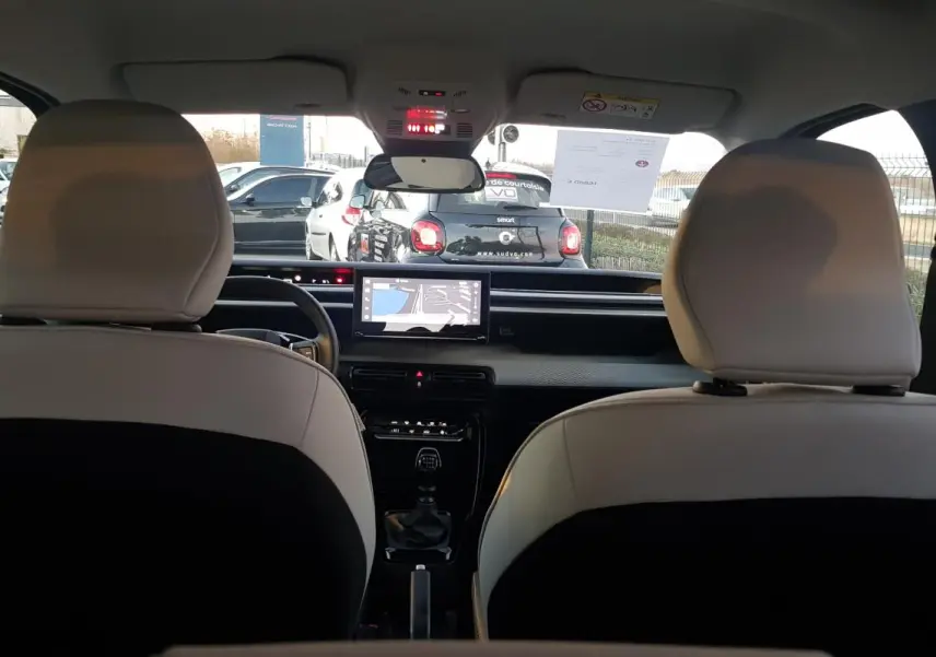 Vue intérieure arrière montrant les sièges bicolores noirs et blancs et la console centrale avec écran tactile de la Citroën C3 noire.