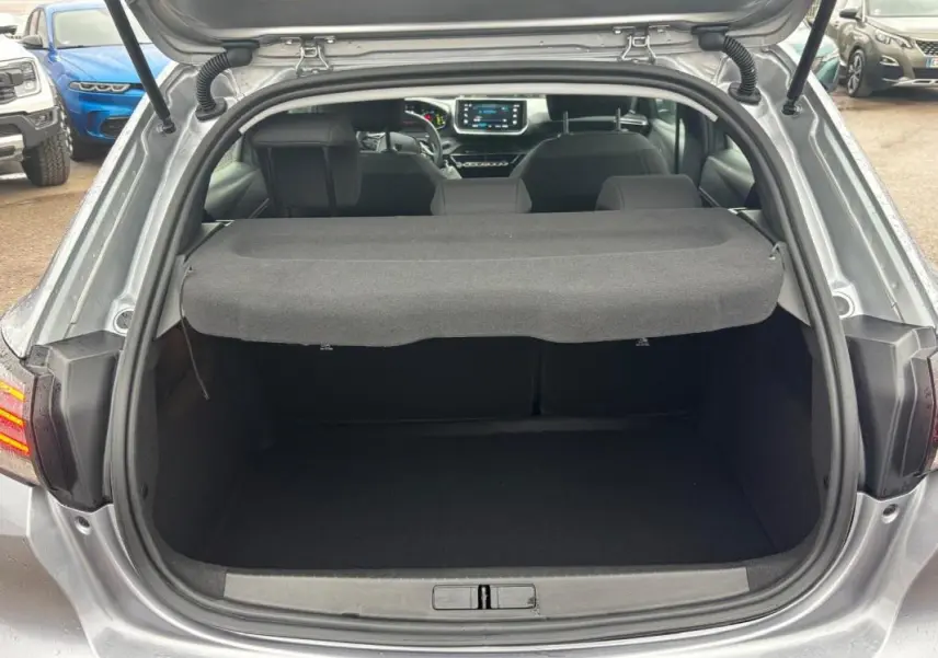Coffre ouvert d'une Peugeot 208 Hybrid gris 2025, vue arrière montrant l'habitacle et l'écran tactile du tableau de bord.