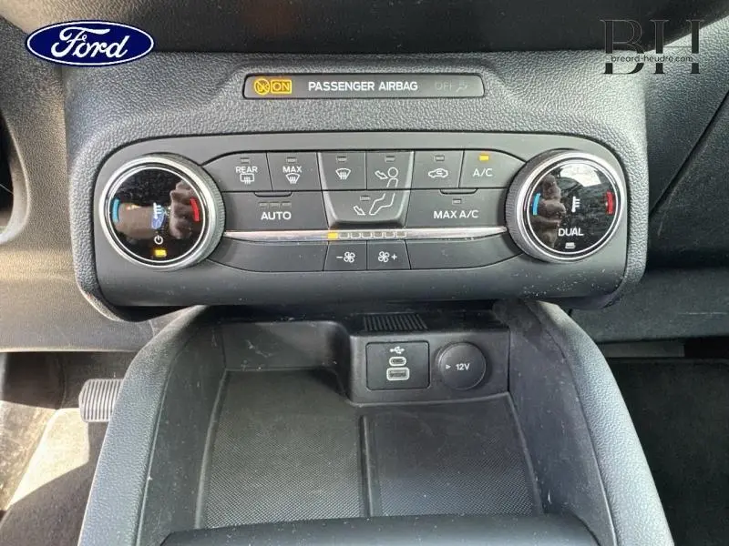 Gros plan sur la console centrale du Ford Kuga 2023, montrant les commandes de climatisation bi-zone et prises USB/12V.