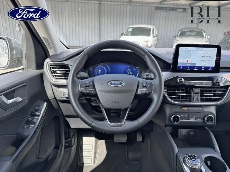 Vue intérieure avant du Ford Kuga 2023, volant cuir multifonction et écran tactile GPS au centre du tableau de bord.