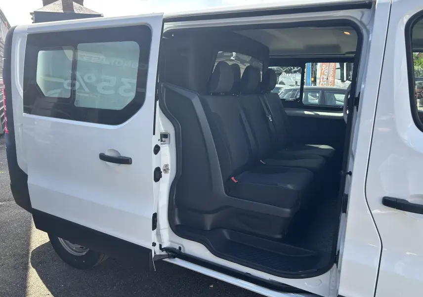 Vue latérale gauche du Renault Trafic blanc avec porte coulissante ouverte, montrant la banquette arrière 3 places en tissu noir.