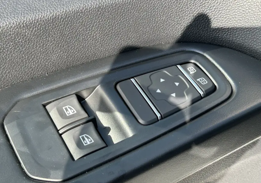 Gros plan sur les commandes de lève-vitres et réglage des rétroviseurs côté conducteur du Renault Trafic blanc.