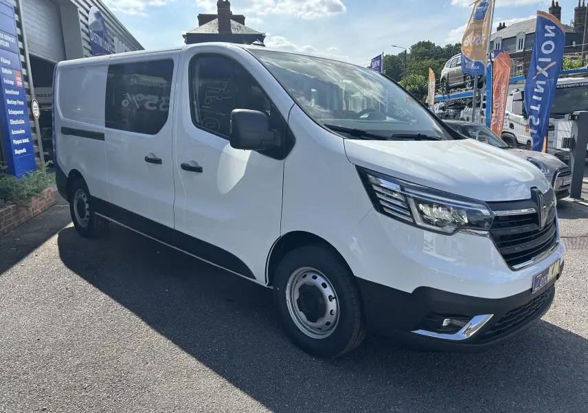Vue 3/4 avant droit d’un Renault Trafic cabine approfondie blanc avec portes latérales coulissantes et projecteurs modernes.
