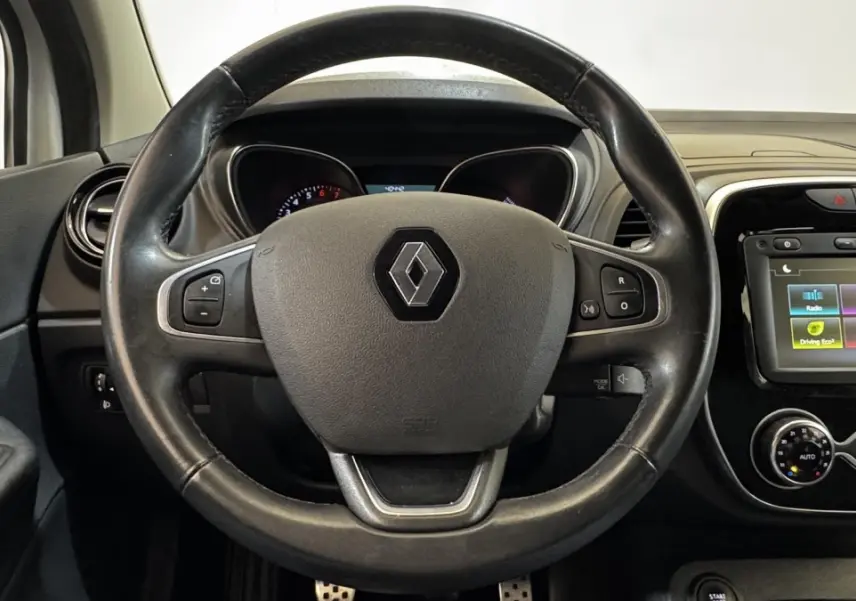 Vue intérieure centrée sur le volant cuir multifonctions et l'écran tactile du tableau de bord du Renault Captur blanc.