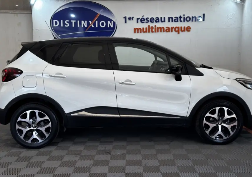 Profil droit du Renault Captur blanc 2019 avec toit noir et jantes alliage bicolores, stationné en intérieur.