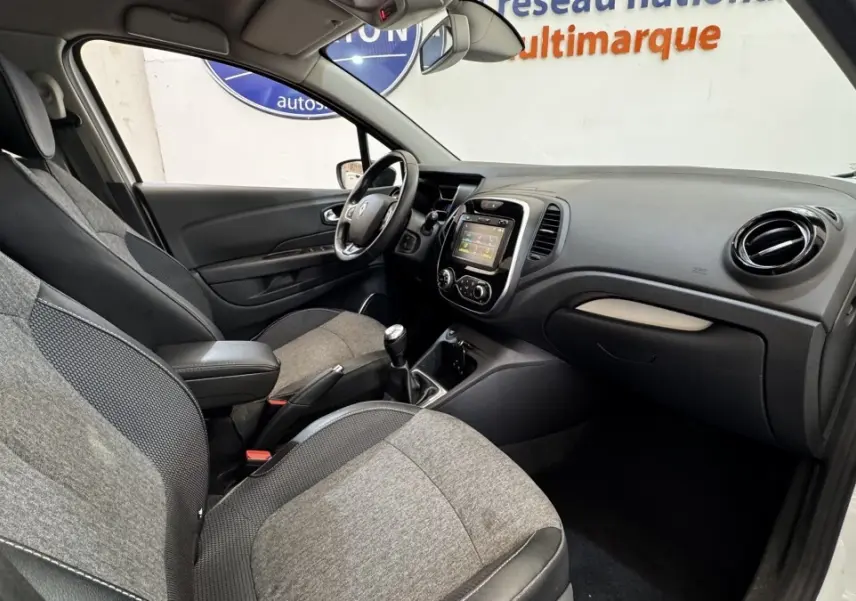 Vue intérieure côté conducteur du Renault Captur blanc 2019, montrant tableau de bord et sièges gris bi-matière.