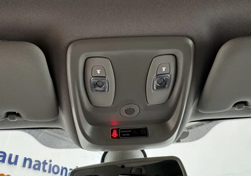 Plafonnier intérieur gris avec deux lampes de lecture et témoin airbag passager allumé dans un Renault Captur blanc.