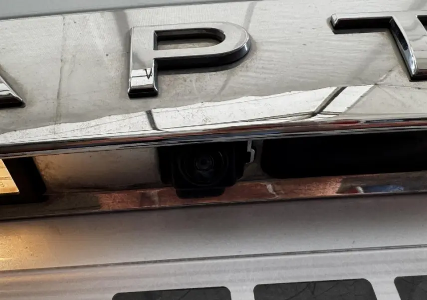 Gros plan sur la caméra de recul intégrée sous le logo chromé "CAPTUR" d'un Renault Captur blanc.