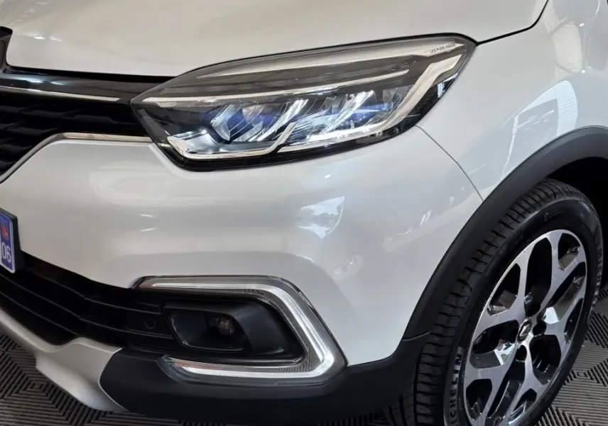Gros plan sur l'avant droit blanc d'un Renault Captur Intens 2019, mettant en valeur le phare LED et la jante alliage.