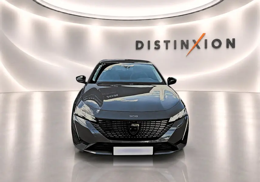 Vue frontale d'une Peugeot 308 gris selenium 2025 avec calandre noire et logo distinctif dans un showroom lumineux.