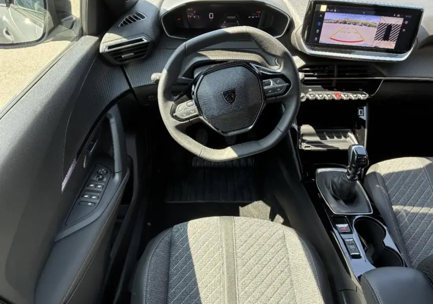Vue intérieure de face du poste de conduite du Peugeot 2008 2024, volant compact, écran tactile avec caméra de recul et levier de vitesse manuel.