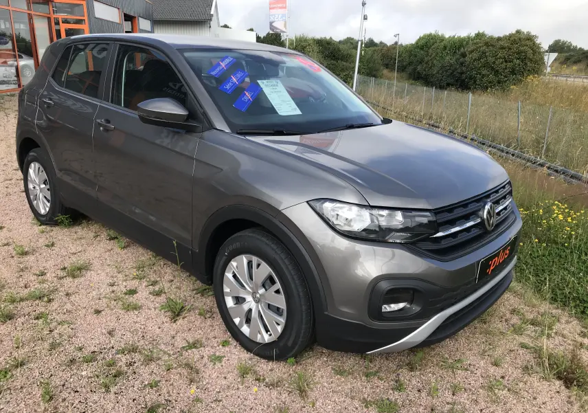 Vue 3/4 avant droit d'un Volkswagen T-Cross 2020 gris limestone, avec jantes alliage et stickers sur le pare-brise.