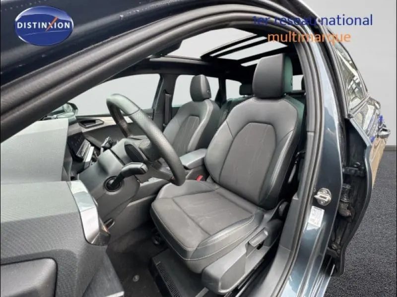 Intérieur de la CUPRA Leon 2024 en gris magnétique mat, vue côté conducteur avec sièges en tissu noir et toit ouvrant panoramique.