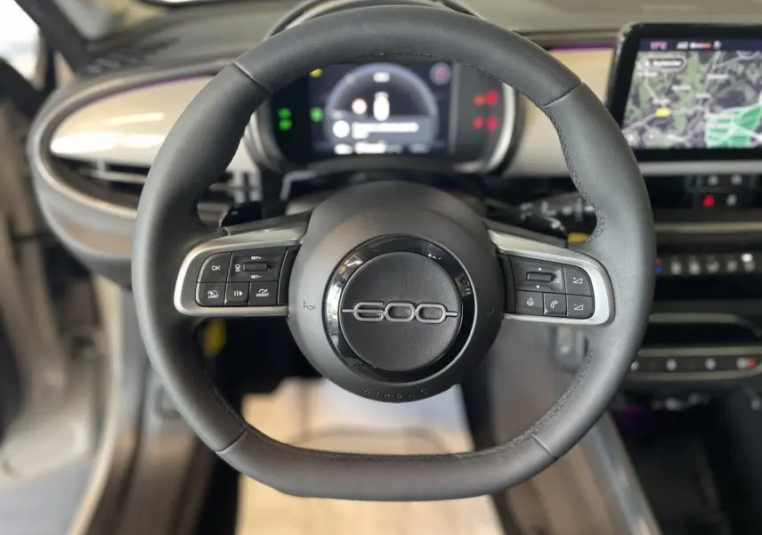 Volant noir du Fiat 600 1.2 Hybrid 2025 avec commandes intégrées et tableau de bord numérique en arrière-plan