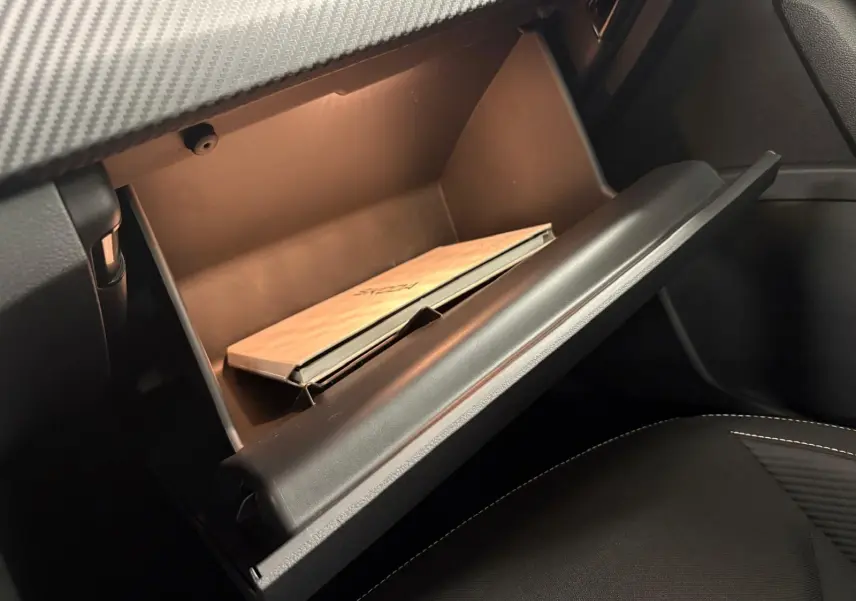 Gros plan sur la boîte à gants ouverte du Skoda Kamiq 2024 Monte Carlo, avec manuel à l'intérieur et sellerie noire visible.