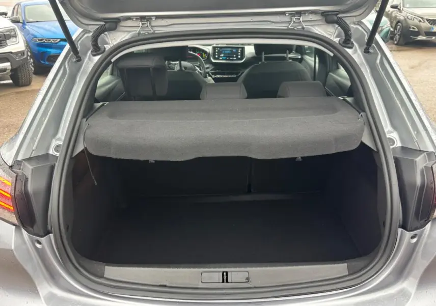 Coffre ouvert d’une Peugeot 208 Hybrid gris 2025, vue arrière montrant l’habitacle et l’écran tactile du tableau de bord.