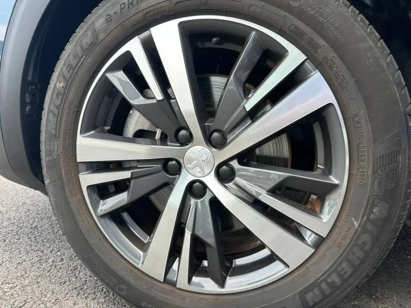 Gros plan sur la jante alu bicolore et le pneu Michelin d’un Peugeot 3008 Hybride Rechargeable bleu côté gauche.