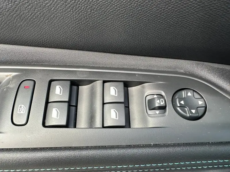 Gros plan sur les commandes des vitres électriques et rétroviseurs du côté conducteur, finition tissu noir avec surpiqûres bleues.