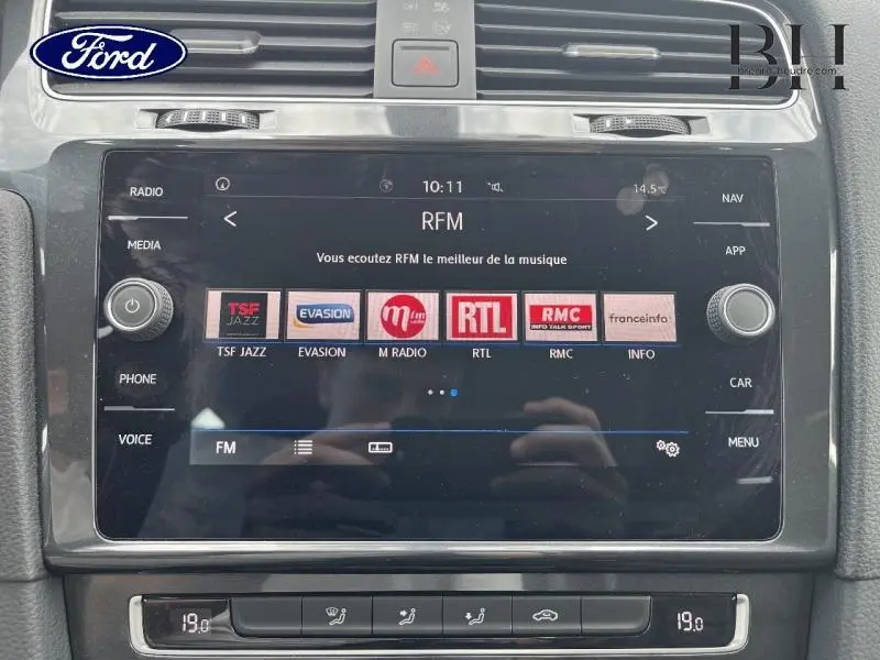 Gros plan sur l’écran tactile multimédia noir du Volkswagen Golf SW gris Tungsten, affichant les stations radio FM.
