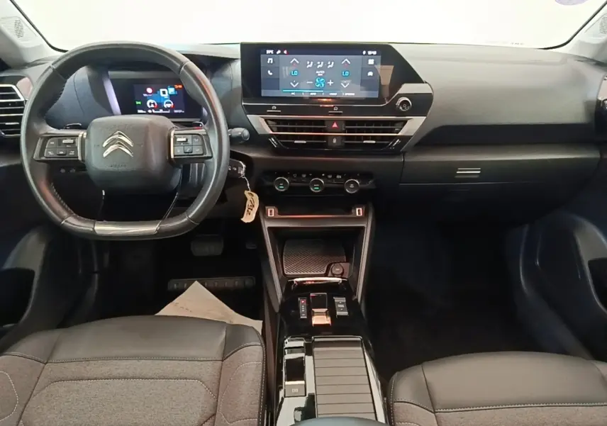 Vue intérieure avant de la Citroën C4 X 2023, tableau de bord noir avec écran tactile central et volant cuir multifonctions.