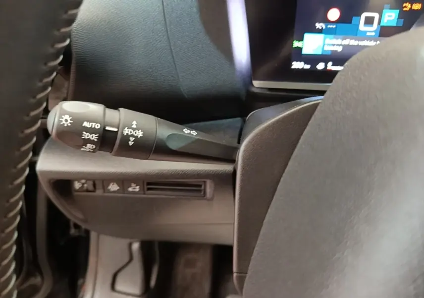 Gros plan sur la commande des phares et clignotants à gauche du volant cuir du Citroën C4 X noir, tableau de bord numérique visible.
