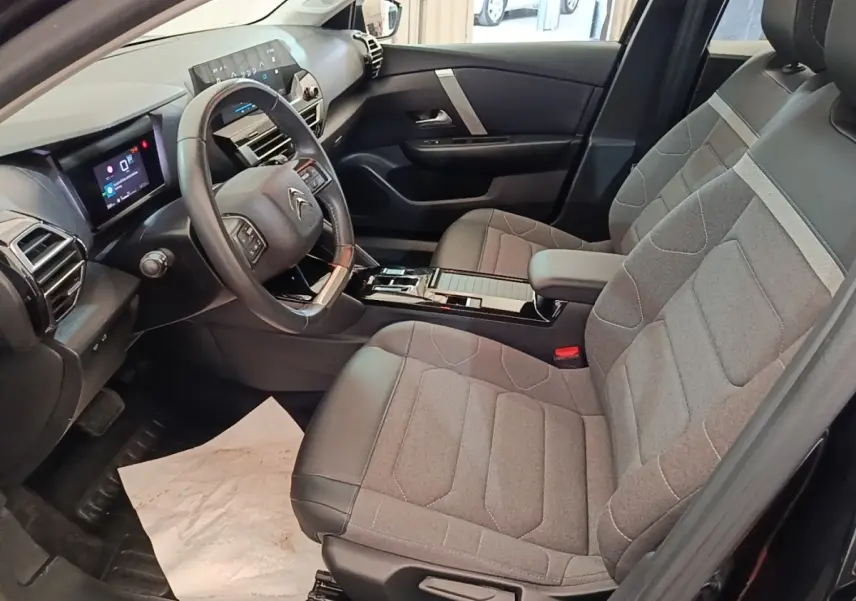 Vue intérieure côté conducteur de la Citroën C4 X noire 2023 avec volant cuir multifonctions et sièges tissu gris.