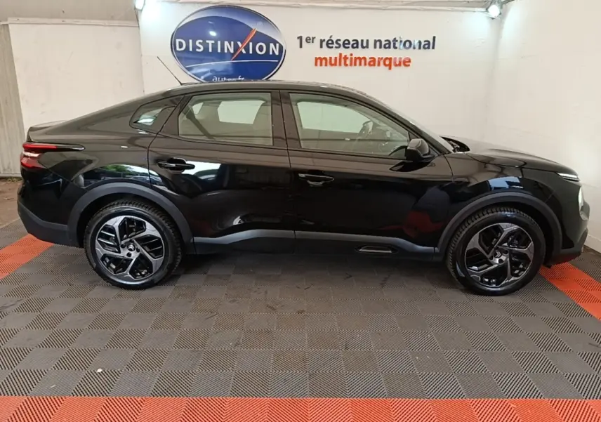 Vue de profil côté gauche d'une Citroën C4 X noire 2023 avec jantes noires et toit légèrement incliné.
