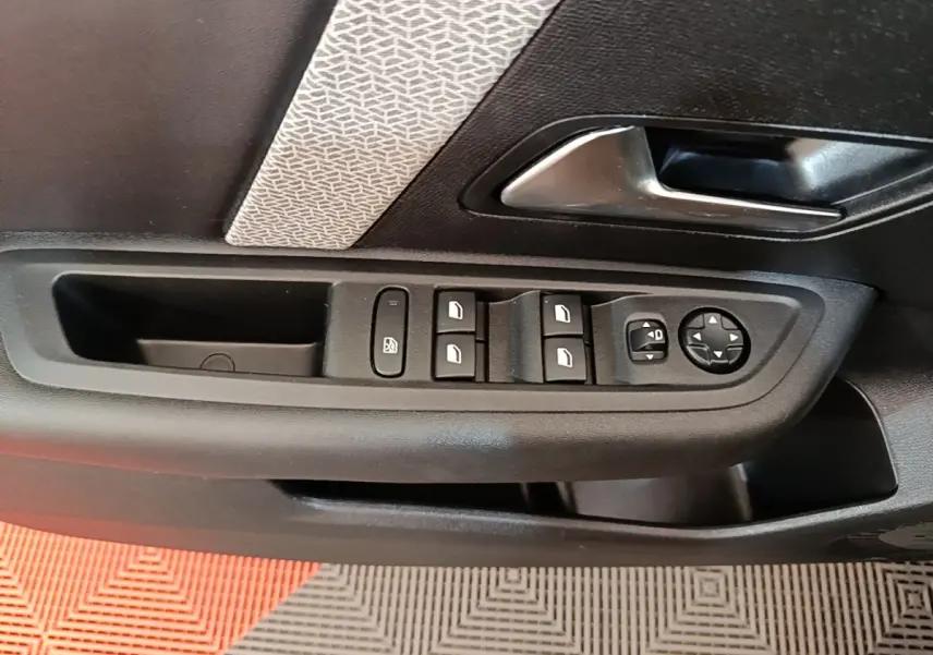Gros plan sur la commande des vitres et rétroviseurs côté conducteur dans une porte intérieure noire avec insert décoratif gris.